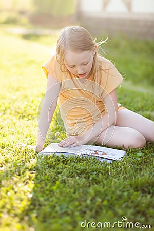 Beautiful teenage girl reading book and sitting on green grass Stock Photo