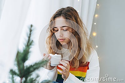 Beautiful teenager girl with cup of cacao with marshmallow sitting on windowsill in the cozy room Stock Photo