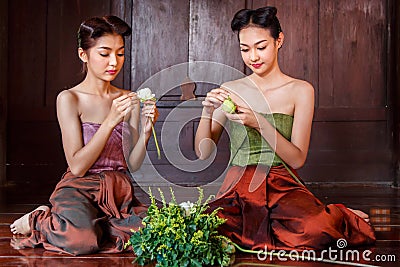Beautiful Thai girls in thai traditional costume trying to roll up lotus flower Stock Photo