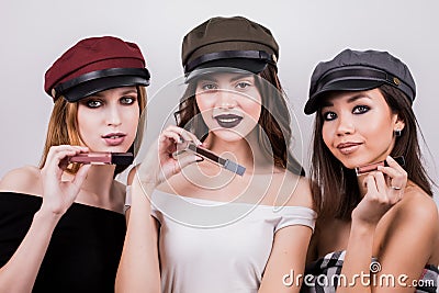 Beautiful three women with makeup and in caps advertise lipstick, lip gloss. Beauty, fashion, fashion, cosmetics products. Stock Photo