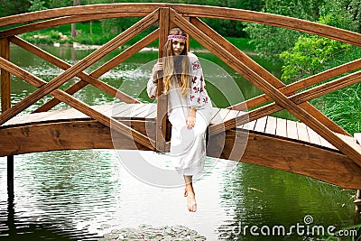 Steep slender Ukrainian woman resting sitting on a wooden decorative bridge over the water on a hot sunny day Stock Photo