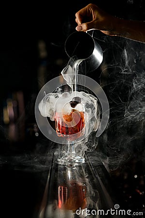 Beautiful view on hand of girl bartender pouring steaming liquid from steel mixing cup into drinking glass Stock Photo