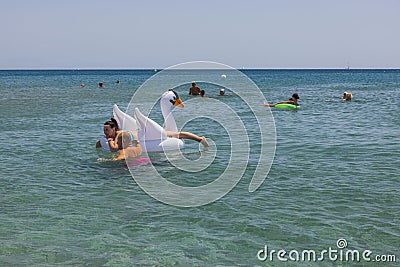 Beautiful view of people swimming in sea. Couple on inflatable white swan on front. Editorial Stock Photo