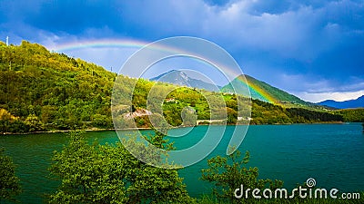 A beautiful view of the spring landscapes and a rainbow over the lake. Dark clouds in the background. Stock Photo