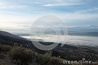 Beautiful view of Umbria valley in a winter morning, with fog covering trees and houses and olive plants in the Stock Photo