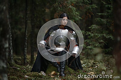 A beautiful warrior girl with a sword wearing chainmail and armor in a mysterious forest. Stock Photo