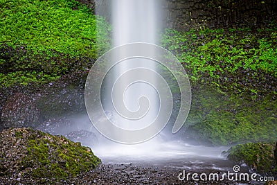 A beautiful waterfall splashing into a pool beneath rocks covered in lush green moss and vegetation Stock Photo
