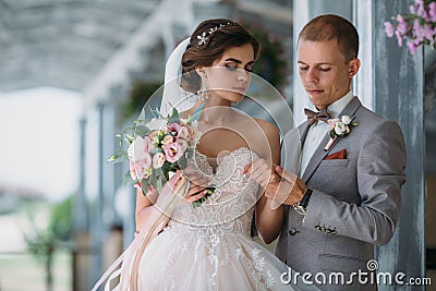 Beautiful wedding couple hugging in park with green trees on background. Groom in a business gray suit, white shirt in a Stock Photo