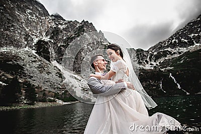 Beautiful wedding photosession. The groom circles his young bride, on the shore of the lake Morskie Oko. Poland Stock Photo