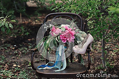 Beautiful wedding shoes with high heels and a bouquet of colorful flowers on a vintage chair on the nature Stock Photo