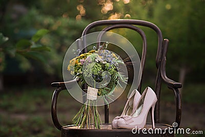 Beautiful wedding shoes with high heels and a bouquet of colorful flowers on a vintage chair on the nature in sunset light Stock Photo