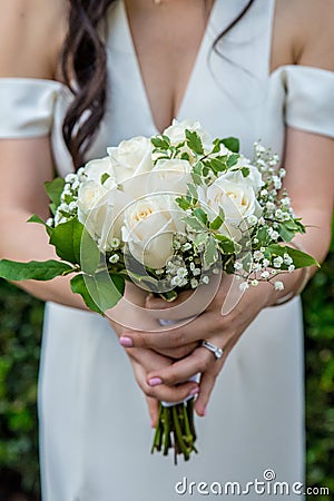 Beautiful white rose bouquet with baby`s breath held by a bride with dark hair wearing a white wedding dress and an engagement rin Stock Photo