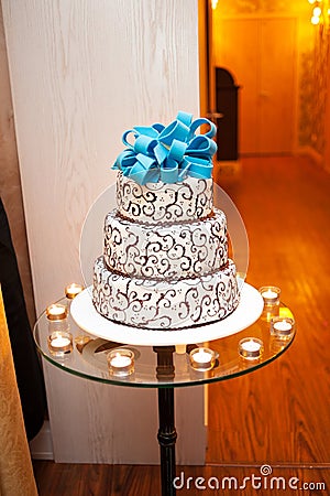 Beautiful white three-tier cake with a turquoise bow on top is on the table Stock Photo
