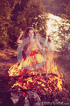 Beautiful witch in the woods near the fire. Magic woman celebrating Halloween. Girl doing witchcraft in the forest. Stock Photo