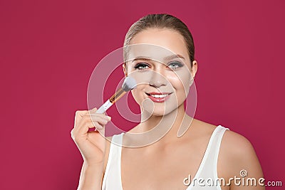 Beautiful woman applying makeup with brush on pink background Stock Photo