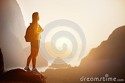 Beautiful woman with backpack at sunrise or sunset on mountain top Stock Photo