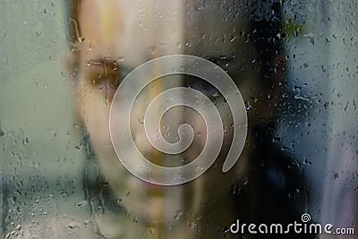 Beautiful woman behind the glass with water drops looking directly at camera. Girl takes a shower, voyeurism Stock Photo