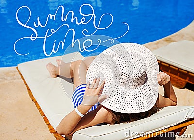 Beautiful woman in a big white hat on a lounger by the pool and text Summer time. Calligraphy lettering hand draw Stock Photo