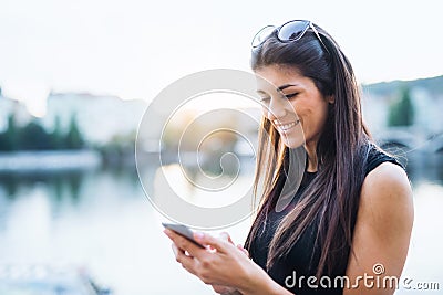 Beautiful woman in black dress standing by a river in city of Prague, text messaging. Stock Photo