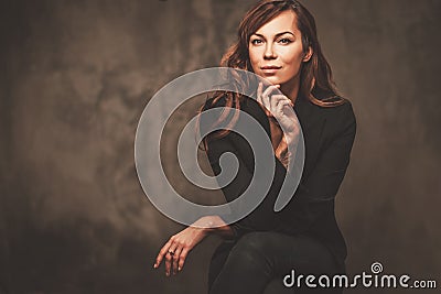Beautiful woman in black sitting on chair isolated on gray background. Stock Photo
