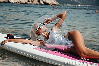 Beautiful woman with blond hair in elegant swimming suit posing with surfer board in the sea Stock Photo