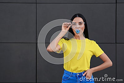 Beautiful woman blowing gum near dark tiled wall outdoors, space for text Stock Photo