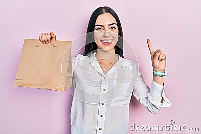 Beautiful woman with blue eyes holding take away paper bag smiling with an idea or question pointing finger with happy face, Stock Photo