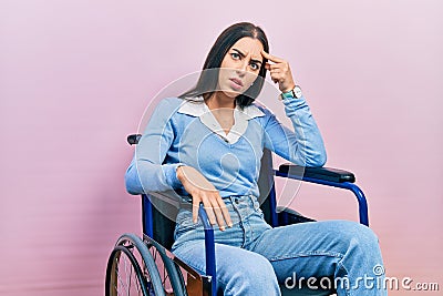 Beautiful woman with blue eyes sitting on wheelchair pointing unhappy to pimple on forehead, ugly infection of blackhead Stock Photo