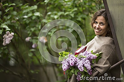 beautiful woman with a bouquet of lilacs and a book in his hands, in the open air among the greenery. Stock Photo