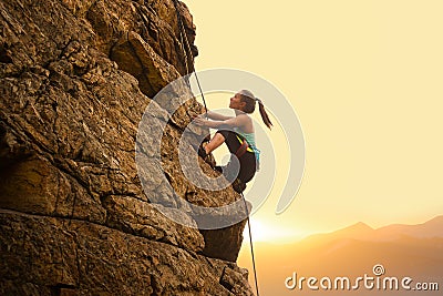 Beautiful Woman Climbing on the Rock at Foggy Sunset in the Mountains. Adventure and Extreme Sport Concept Stock Photo