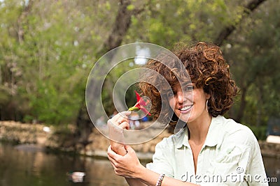 Beautiful woman with curly hair sitting on a duck and swan pond in the park. The woman is happy and holds a red flower in her hand Stock Photo