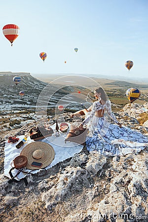 Beautiful woman with dark hair in elegant dress having picnic with fantastic view on valley with air balloons on background Stock Photo