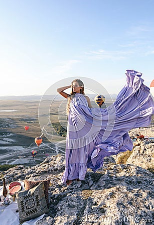 Beautiful woman with dark hair in elegant dress having picnic with fantastic view on valley with air balloons on background Stock Photo