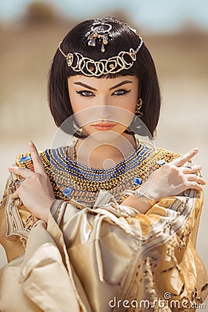 Beautiful woman with fashion make-up and hairstyle like Egyptian queen Cleopatra outdoors against desert Stock Photo