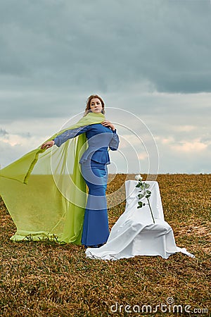 Beautiful woman in the field in blue dress and yellow veil. there is chair in the clearing Stock Photo