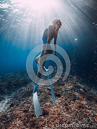 Beautiful woman with fins glide underwater in blue sea. Freediving with sporty girl in ocean and sun rays Stock Photo