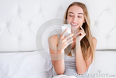 Beautiful woman flirts on the phone while sitting in bed at the hotel Stock Photo