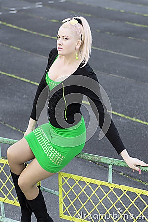 The beautiful woman in green sits on a protection of stadium Stock Photo