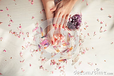 Beautiful woman hands with perfect violet nail polish on white wooden background holding little quartz crystals Stock Photo