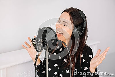 Beautiful woman in headphones sings a song near a microphone in a recording studio. Place for text or advertising Stock Photo