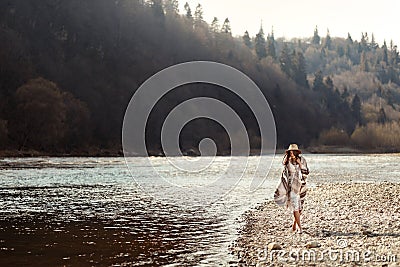 beautiful woman hipster walking on river beach in mountains,wearing hat and poncho, boho travel concept, space for text Stock Photo