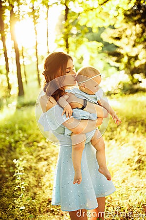 Beautiful woman hold little baby girl in caring arms, walking at the park, hugging, lovely mother kissing adorable Stock Photo