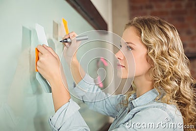 Beautiful woman holding sticky note while writing on glass board Stock Photo