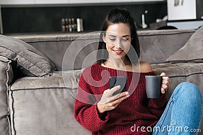 Beautiful woman indoors in home using mobile phone drinking coffee Stock Photo