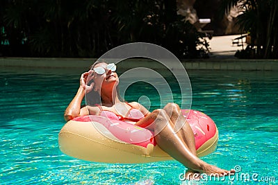 Beautiful woman and inflatable swim ring in shape of a donut in the pool. Stock Photo