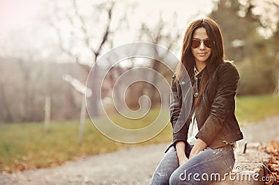 Beautiful woman in jacket and jeans sitting in a park Stock Photo