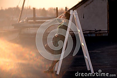 Beautiful woman leaning on white ladder on rooftop Stock Photo