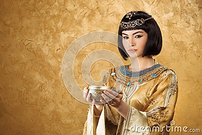 Beautiful woman like Egyptian Queen Cleopatra with cup on golden background Stock Photo