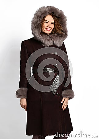 Beautiful woman with long curly red hair in black sheepskin coat with fur-trimmed hood and wide leather belt on white Stock Photo