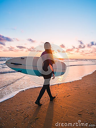 Beautiful woman with long hair go to surfing. Surfgirl with surfboard on a beach at sunset or sunrise. Surfer and ocean Stock Photo